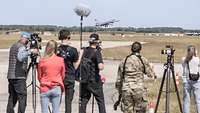 Members of the media photograph a fighter jet taking off.