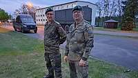 Zwei Soldaten stehen bei Abenddämmerung auf der Wiese neben einer Straße. 