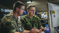 Zwei Soldaten in grünen Uniformen sitzen vor einem Monitor.