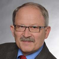 Portraitbild eines Mannes mit kurzer, grauhaariger Frisur, Schnurrbart und Brille.