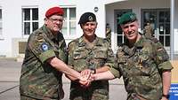 Drei Soldaten stehen vor einem Gebäude und schütteln sich die Hände.