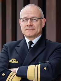 Ein Mann mit verschränkten Armen, steht vor einer Wand.