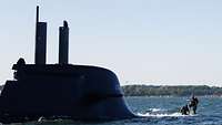 Zwei Personen im Tauchanzug auf einem U-Boot in See.
