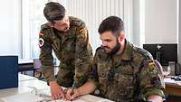 Ein Soldat weist einen anderen Soldaten in einen Ablauf ein und zeigt dabei auf ein Dokument.