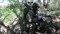 Soldaten knien an einer Waldkante ab und bereiten sich auf einen weiteren Angriff vor.