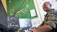 Ein Soldat mit Brille sitzt vor drei Monitoren.