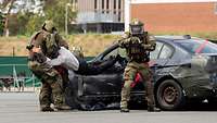 Drei bewaffnete Soldaten in Körperpanzerung ziehen einen Straftäter aus einem Fahrzeug