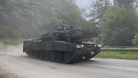 Ein Leopard 2 fährt eine Kurve entlang des Berges hinauf. Er hinterlässt eine Staubwolke. 
