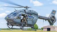 Ein H145M-Hubschrauber schwebt über dem Boden. An der Tür sitzt ein Soldat mit Gewehr.