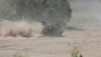 Ein Gefechtsfahrzeug fährt schnell über sandiges Gelände, Sand wirbelt auf.