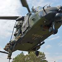 Ein Soldat gleitet an einem dicken Seil von einem schwebenden Hubschrauber auf ein Dach hinunter.