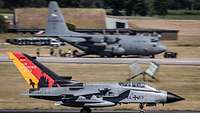 A German jet aircraft is standing in the foreground; in the background, an American transport aircraft can be seen.