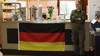 Eine Soldatin steht vor einem Tresen, der mit einer Bundesflagge dekoriert ist. 