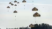 Zahlreiche Fallschirmjäger mit grünen Schirmen schweben nacheinander zum Boden.