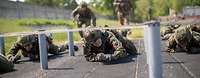 Mehrere Soldaten kriechen unter leicht hoch gespannten Seilen auf einer Hindernisbahn.