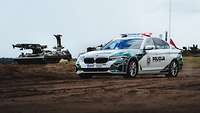 Ein Polizeiwagen am Rand des Übungsgeländes, dahinter Militärfahrzeuge