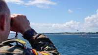 Ein Soldat schaut übers Wasser zu einem U-Boot und einem Hubschrauber