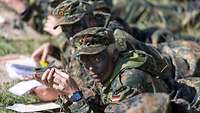 eine Soldatin und ein Soldat liegen mit einem Kompass auf der Wiese