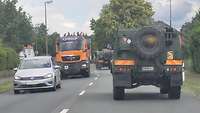 Zwei große militärische Geländewagen fahren auf einer Straße.