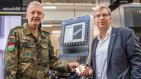 Ein Soldat und ein Zivilisten halten gemeinsam ein Zahnrad in den Händen.