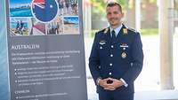 Major Fabian S. steht vor einem Banner. Auf diesem finden sich Informationen über Australien