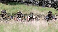 4 Soldaten liegen auf einer hohen Wiese und beobachten etwas