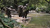 Soldaten gehen durch einen kleinen Fluss, das Wasser geht ihnen bis zu den Knien.