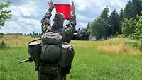 Ein Soldat hält ein rotes Signaltuch hoch, im Hintergrund kommen auf Fahrzeugen die Aufnahmekräfte.