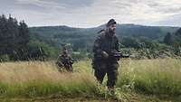 Zwei Soldaten gehen durch hüfthohes Gras.
