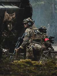 Zwei Soldaten knien hinter einem Schützenpanzer.