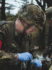 Zwei Sanitäter knien im Wald bei einem Verletzten.
