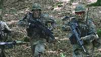 Zwei Soldaten mit Kampfausstattung und Helm rennen durch den Wald.