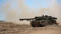 Ein Kampfpanzer Leopard fährt über sandigen Untergrund und wirbelt dabei viel Staub auf.