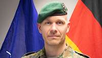 Ein Soldat steht vor einer NATO- und einer Deutschland-Flagge.