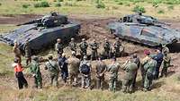 Attachés und acht Panzergrenadiere in der Mitte, links und rechts davon je ein Schützenpanzer Puma.