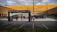 Mehrere Menschen besichtigen eine Open-Air-Ausstellung im Ehrenhof des Flughafen Tempelhof.