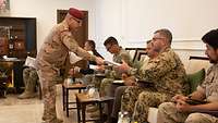 Soldaten aus verschiedenen Nationen sitzen auf Polstermöbeln und erhalten von einem kurdischen Soldaten Unterlagen. 