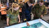 Ein Soldat bedient einem Touchscreen-Tisch. Eine Soldatin und ein Soldat stehen daneben und schauen zu.