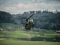 Transporthubschrauber CH-53 Ein Transporthubschrauber CH-53 fliegt dicht über begrünten Boden, im Hintergrund ist ein Wald mit Haus zu erkennen.