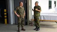 Zwei Soldaten stehen am Eingangstor einer großen Lagerhalle und unterhalten sich.