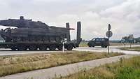 Ein LKW Anhänger auf dem ein Panzer steht fährt über eine Kreuzung.