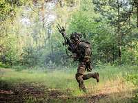 Waldkampf Ein Soldat rennt mit seinem Gewehr im Hochanschlag über eine Freifläche im Wald.