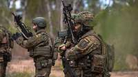 Soldaten stehen mit dem Gewehr nach oben nebeneinander im australischen Buschland.