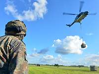 Ein Soldat schaut zu einem fliegenden Hubschrauber vom Typ Sea Lynx Mk88A mit Außenlast hoch