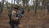 Mehrere Soldaten mit Gewehr laufen mit Waffen in der Hand durch die Buschlandschaft Australiens.