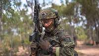Ein Soldat mit Gewehr steht im Outback Australiens und wechselt ein Magazin.