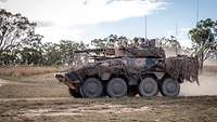 Ein Radpanzer fährt über einen Sandweg im australischen Outback.