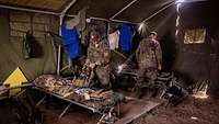 Two soldiers standing near field beds in a large green tent. 