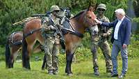 Zwei Soldaten und der Bundespräsident stehen um ein Muli.