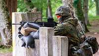 Eine Person im Gefechtsanzug zielt mit einem Gewehr. Das Gewehr liegt auf Sandsäcken auf.